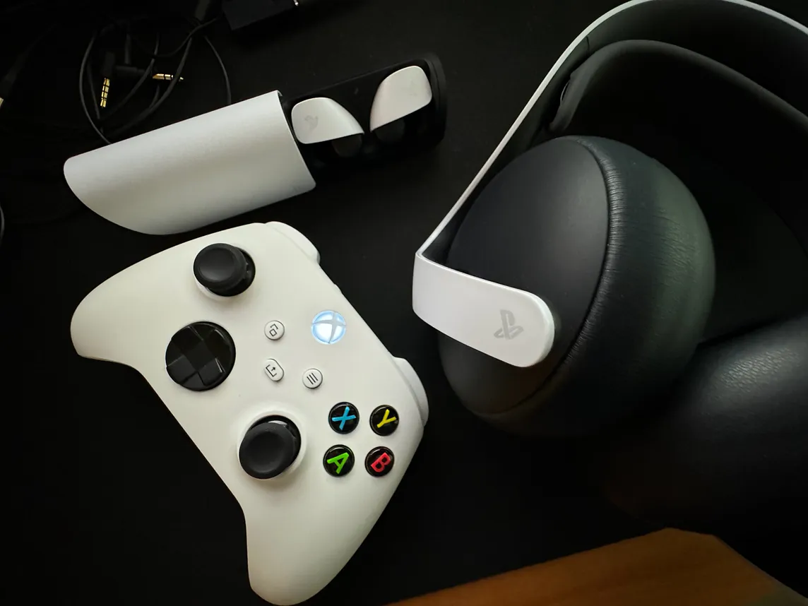 Sony Pulse Explore earbuds and a Pulse Elite gaming headset on a desk next to a powered-on Xbox controller.
