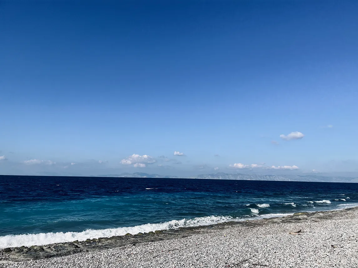 picture of a blue sky above the ocean with small waves approaching the sand.