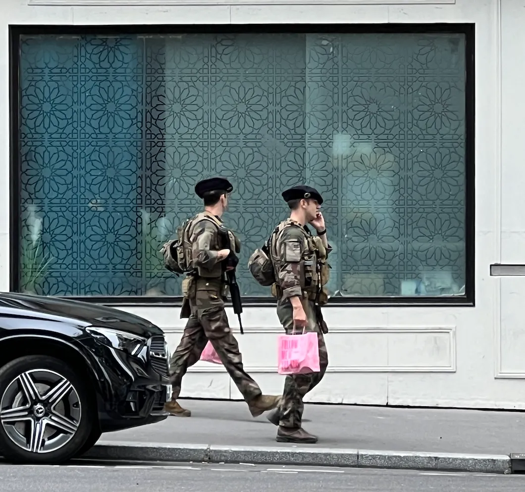 Two soldiers carrying machine guns and pink shopping bags.