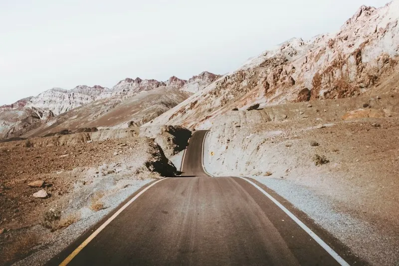 Sepia image of a road running through a barren, but hilly, landscape towards some distant mountains