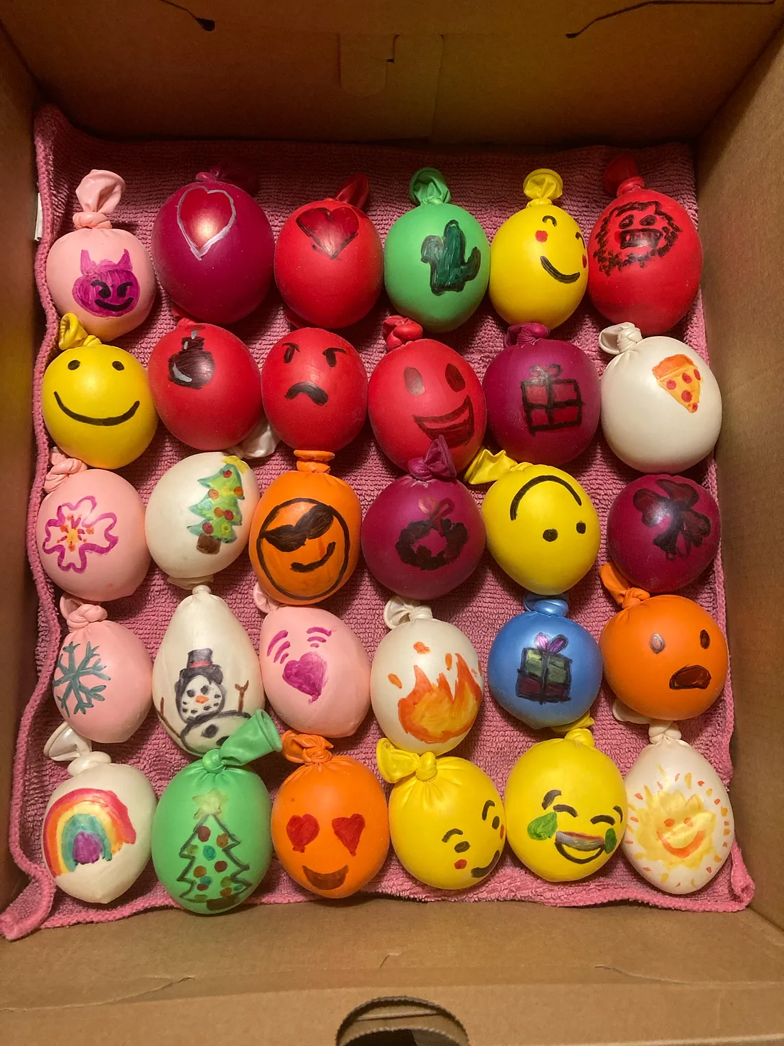 An array of colourful balloons filled with flour made by a team of children with different emojis and faces drawn on them — a loose metaphor for a team or the product of teamwork