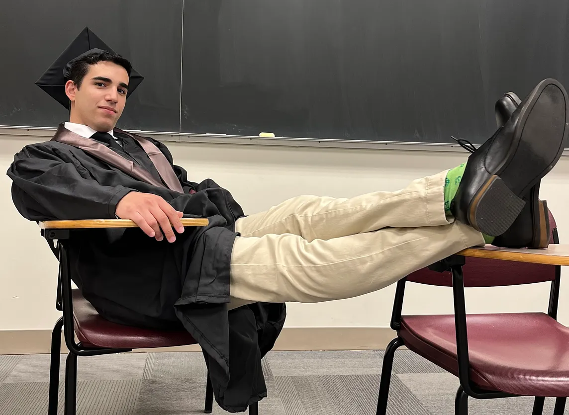 Me with my feet up on a desk wearing my graduation cap and gown