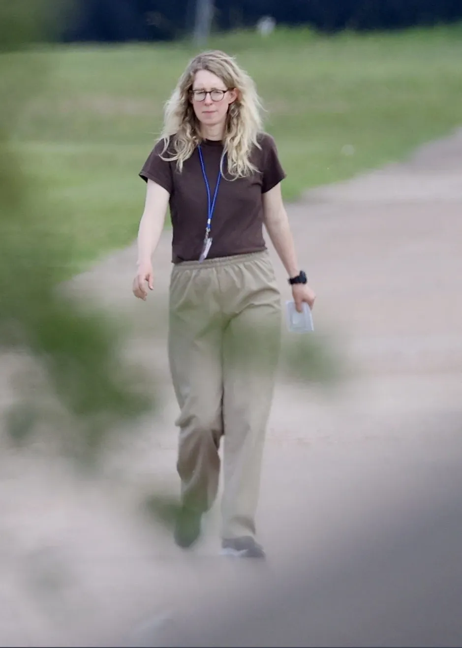 Elizabeth Holmes, in glasses and prison garb, is seen walking toward the camera.