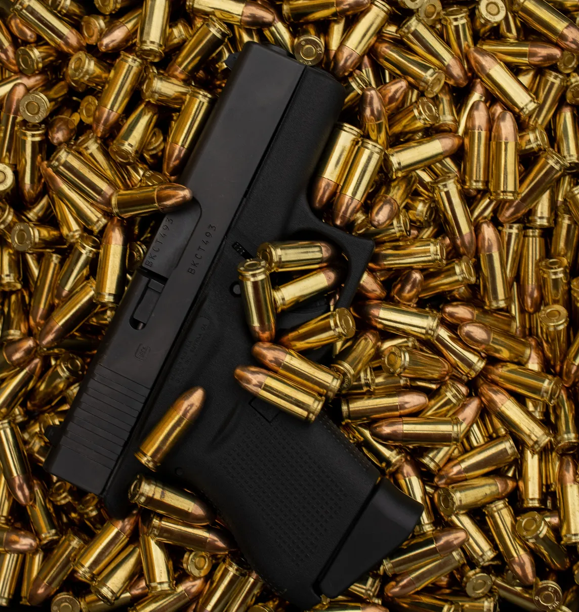 A handgun lies haphazardly amidst an ocean of brass bullets