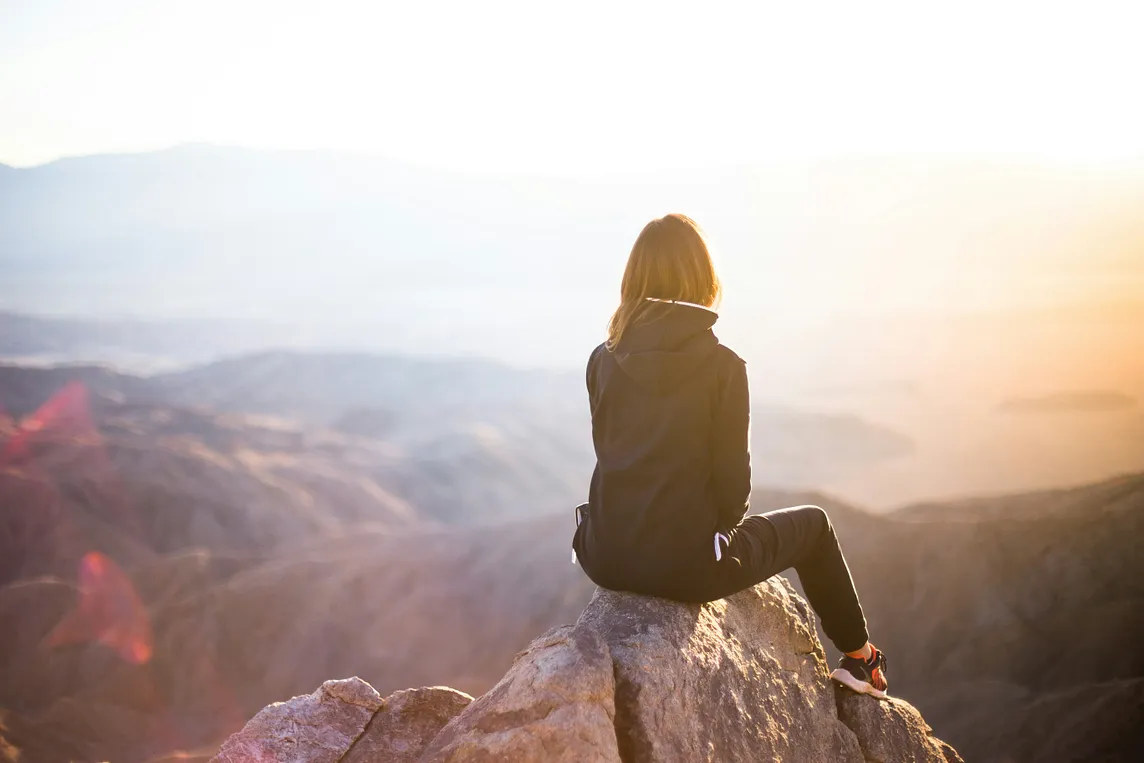 Woman sitting on a mountain top overlooking other mountains.