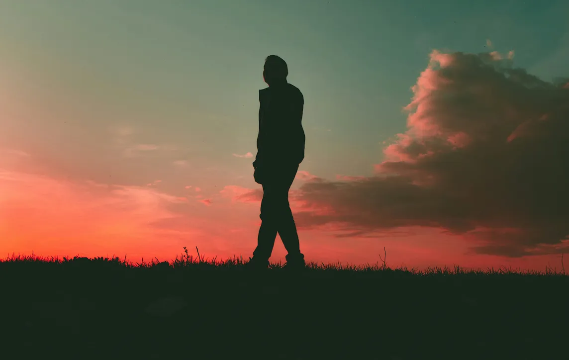 Silhouette of a man at sunset. Pink sky and clouds.