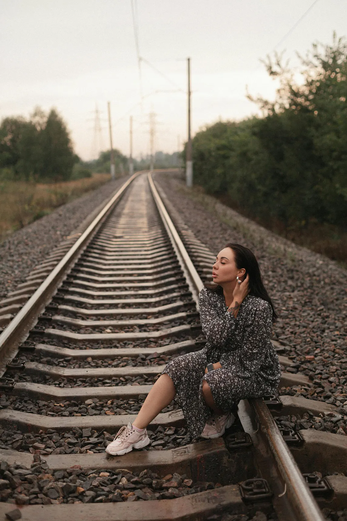 Alt-text: A woman in dark clothing sits on a railway track at dusk, symbolizing crossings between danger and freedom.