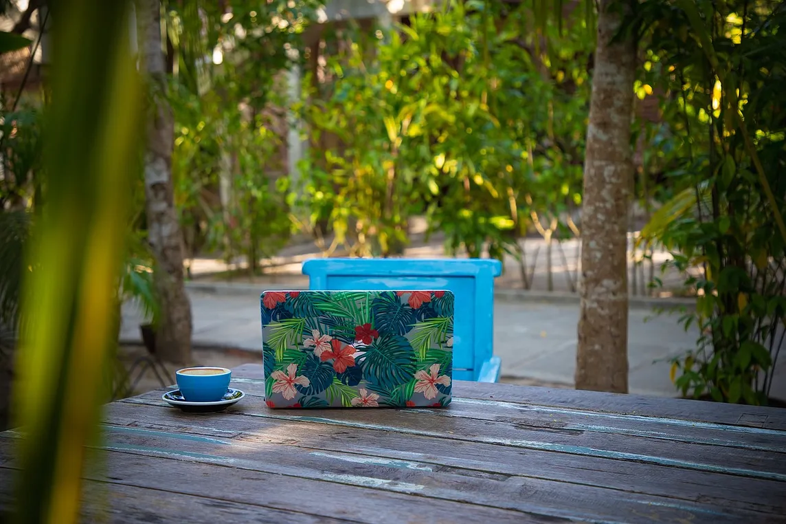 Outdoor setting with a laptop and coffee cup on a table surrounded by trees.