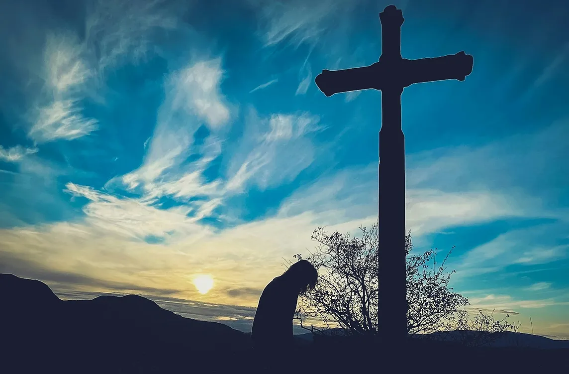 A person kneeling at a cross