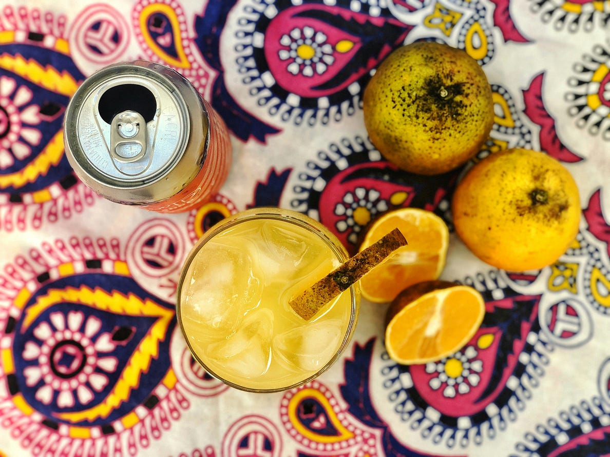 Top-down view of a can, cocktail and several pieces of fruit against a colourful pink and yellow tablecloth