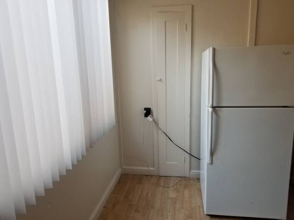 A refrigerator is plugged into an outlet so that its cord obstructs the door of a built-in foldout ironing board.