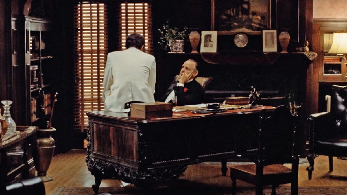The image many Americans carry of concentrated authority comes from films like The Godfather: a single figure at the head of a darkened table, loyalty negotiated in private. Still from The Godfather (1972), Paramount Pictures. Used for commentary on hierarchical power structures.