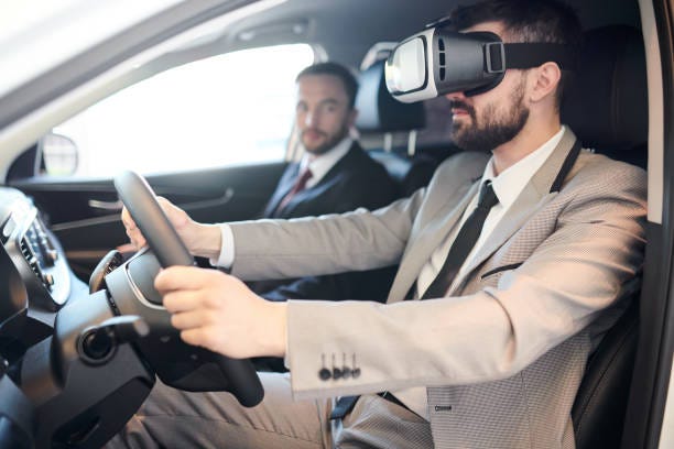 A man using a VR headset while sitting in the front seat of a car with a salesman beside him.