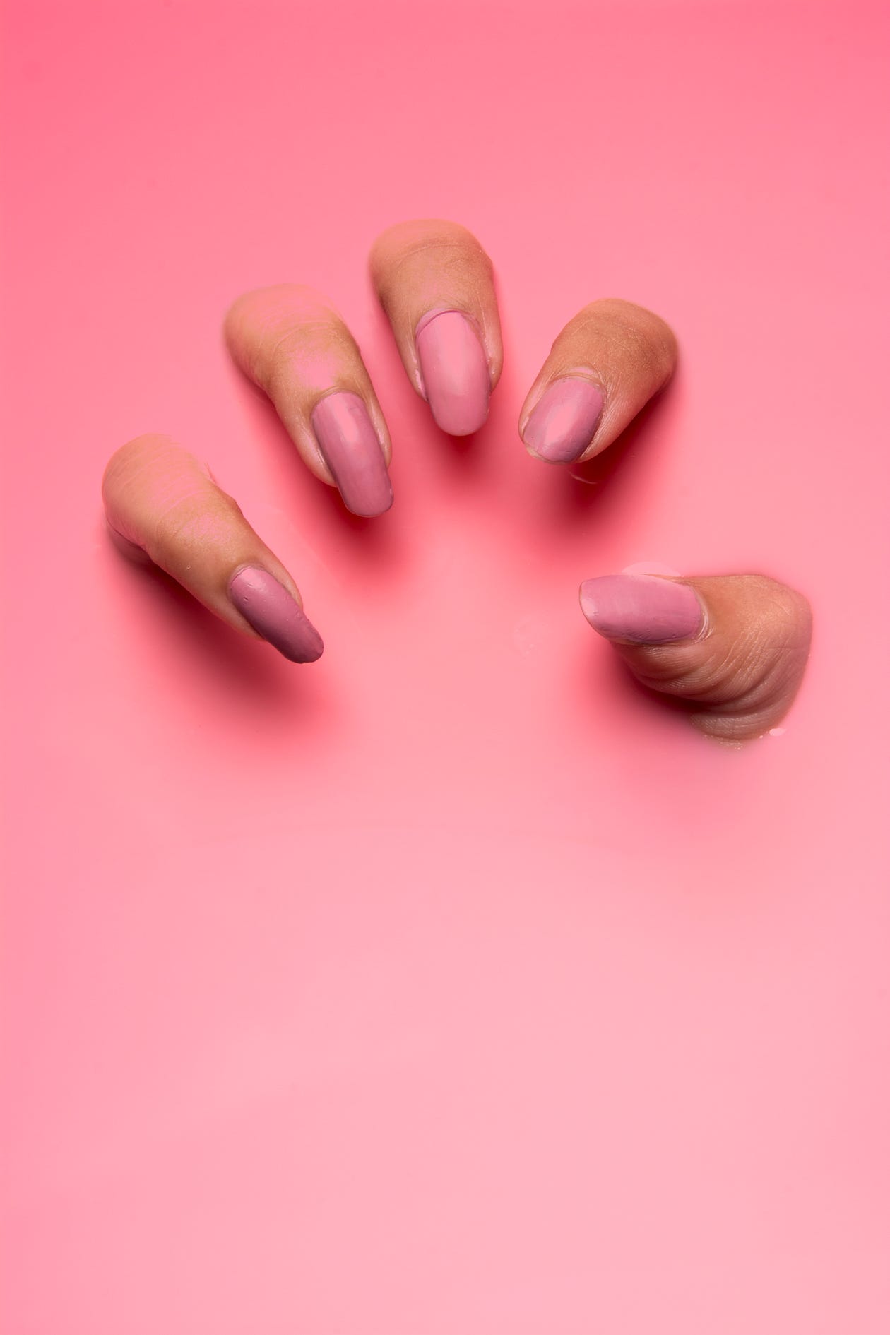 Horribly manicured hand with pink nail polish scratching out of a pink background.