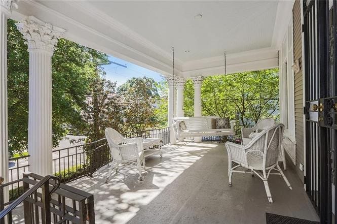 A large porch with white wicker furniture and a white porch swing.