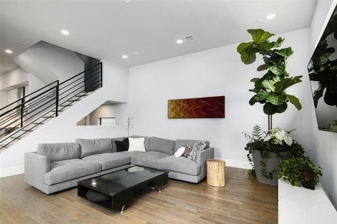 A living room with medium-toned wood floors and a large gray sectional couch + a black coffee table.