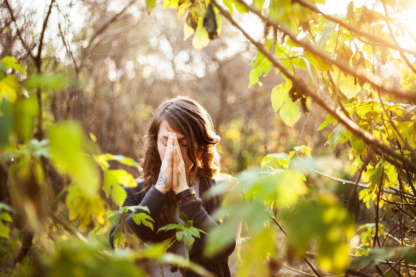 Woman in nature with her hands in prayer pose.