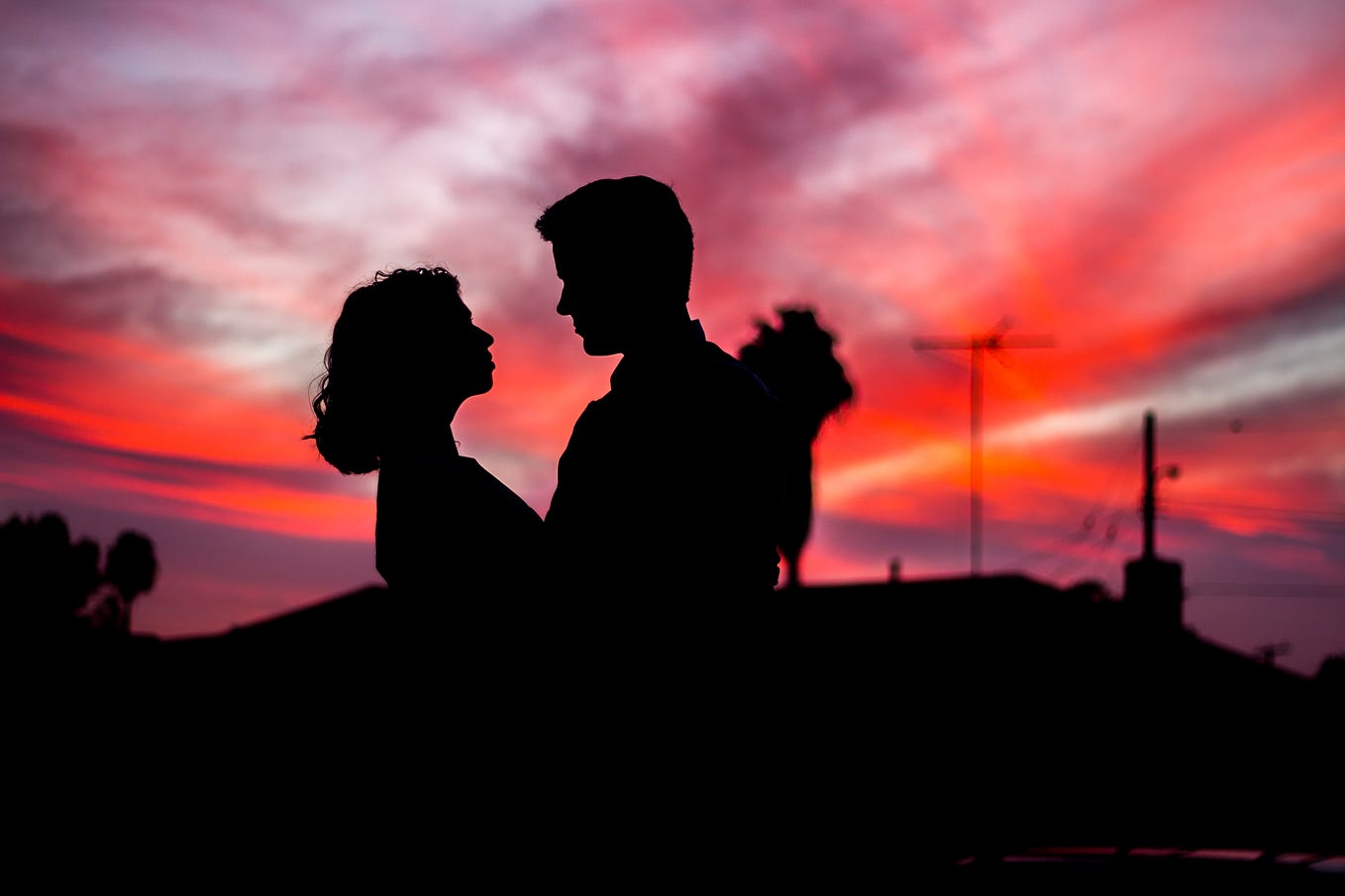 A man and a woman stand facing each other in front of a sunset.