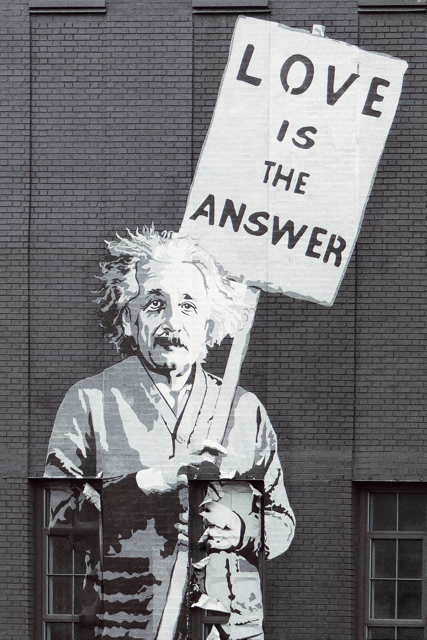 Einstein holding a sign that says “Love is the answer.”