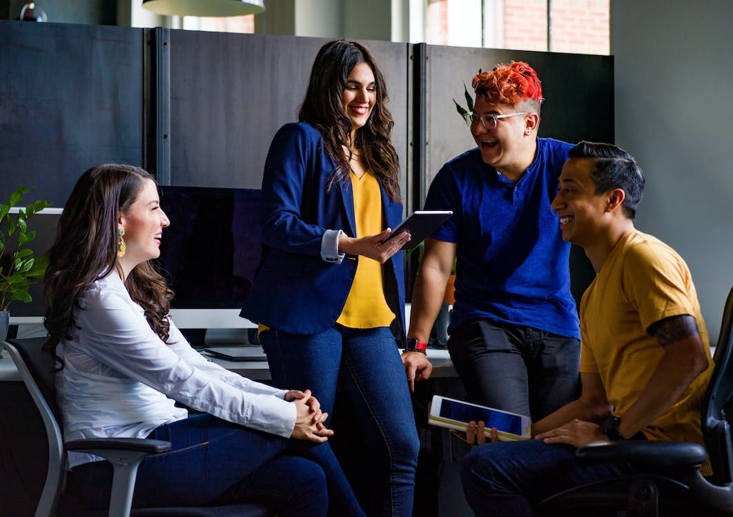 Group of people sitting inside room looking at a tablet, all smiling and enjoying themselves