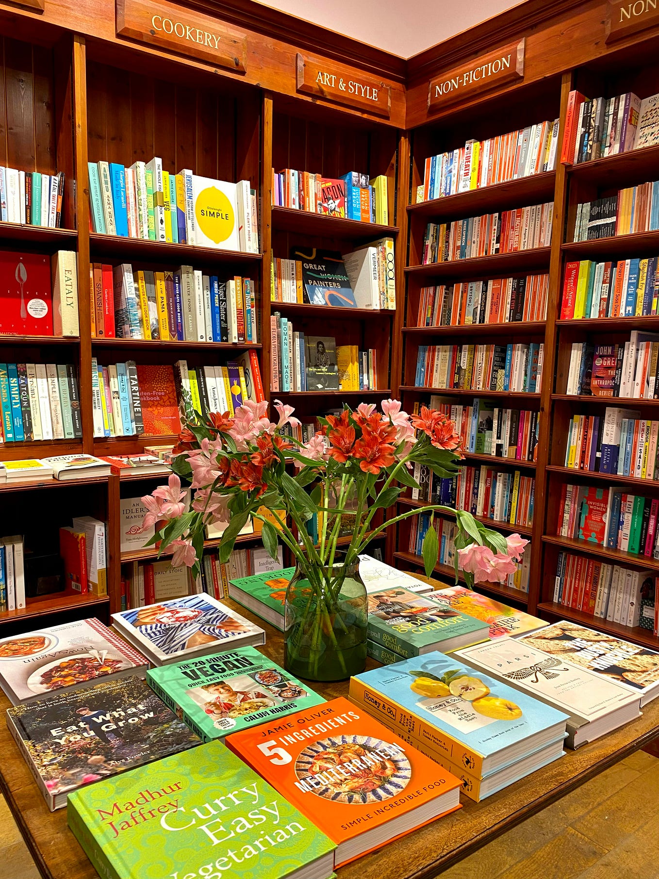 A bookshop’s shelves and table display with flowers in a vase