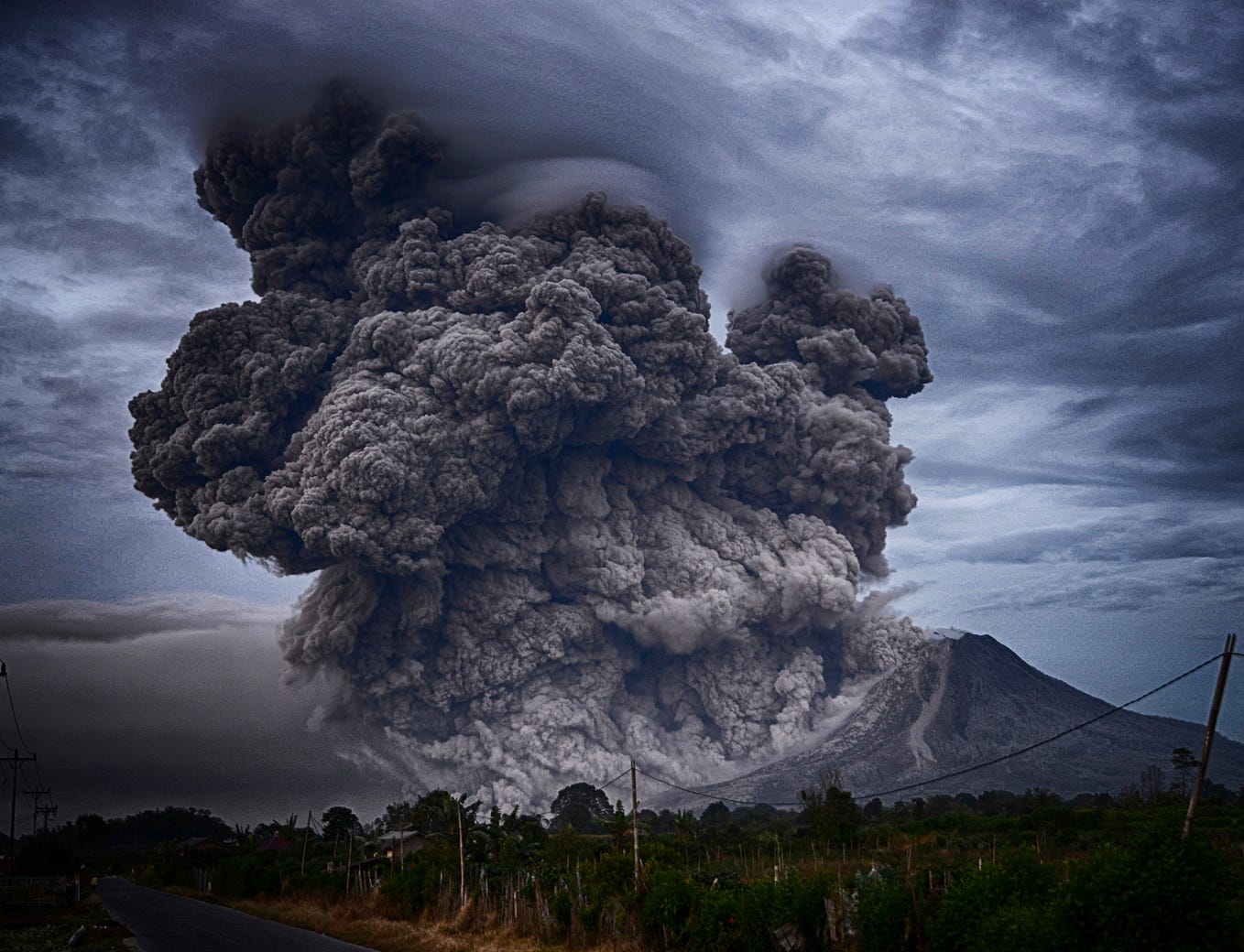 Volcano spews ash under darkened sky.