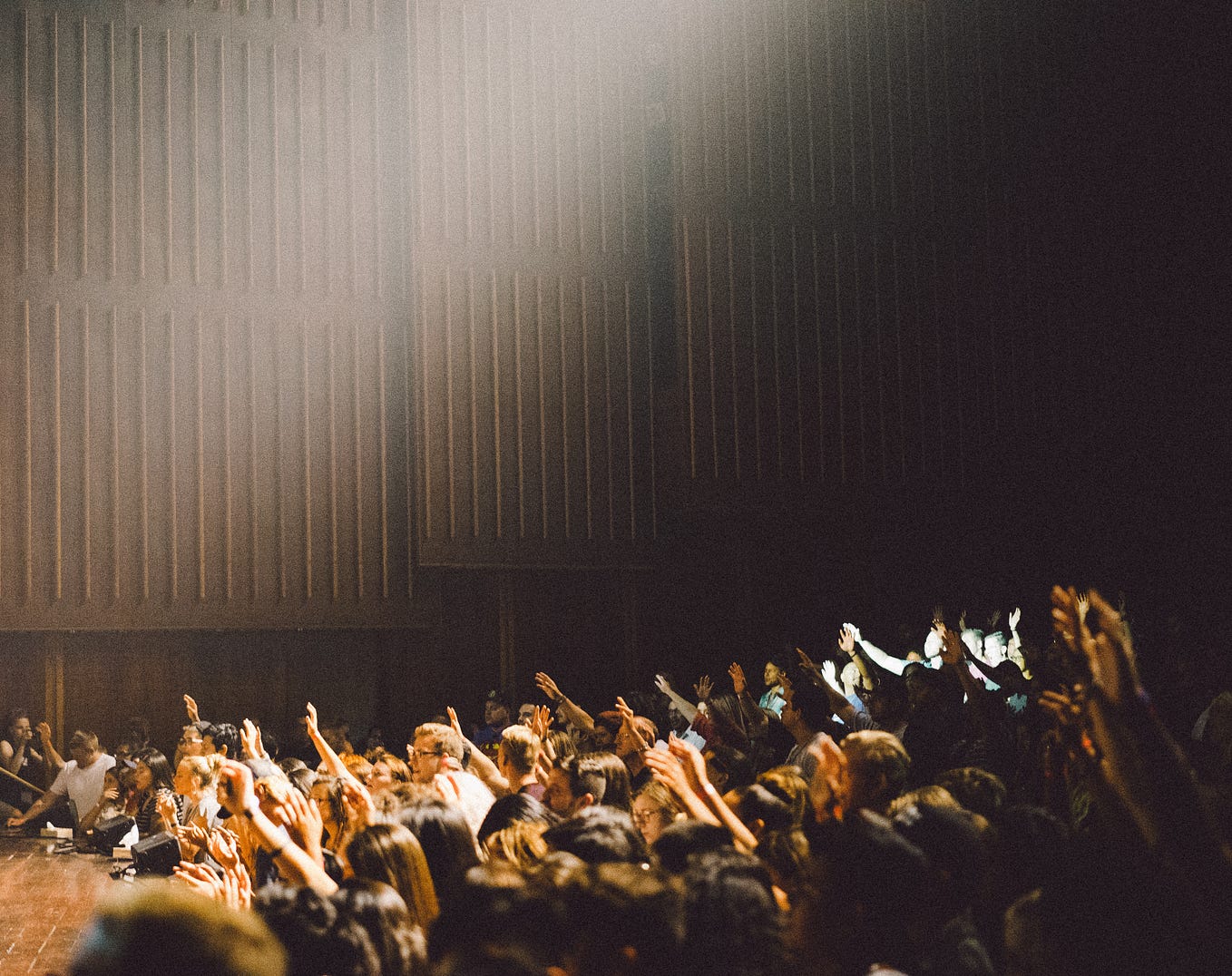 The image shows an ampitheater filled with people who are looking forward and raising their hands as if to respond to a question from the stage (not visible) in front.
