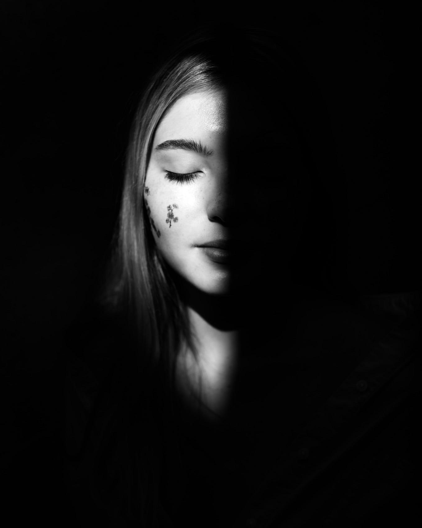 Black and white photo of a female with her eyes gently closed. A black shadow cast, covering half of her face.