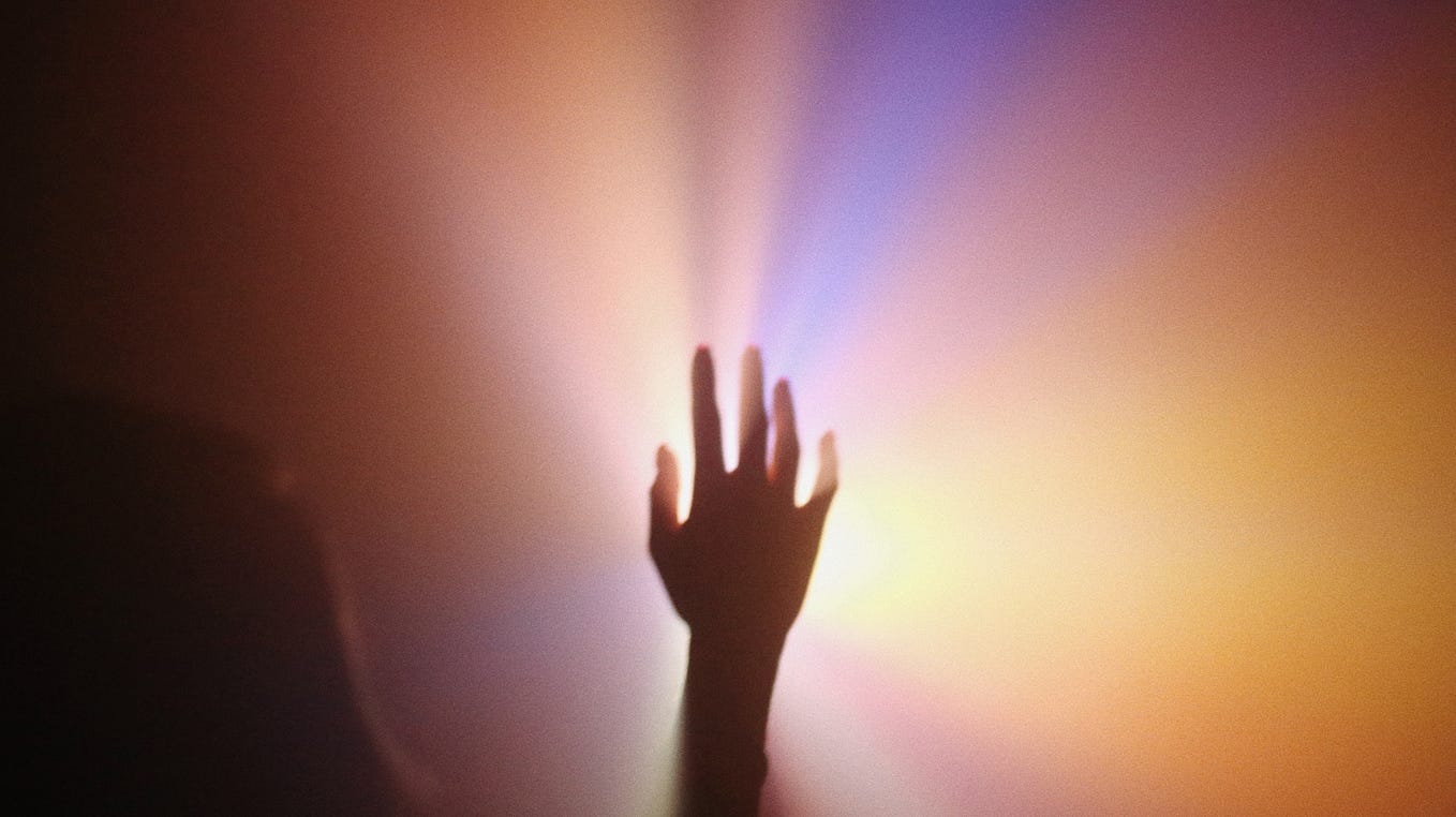 A hand reaching up to a colorful light.