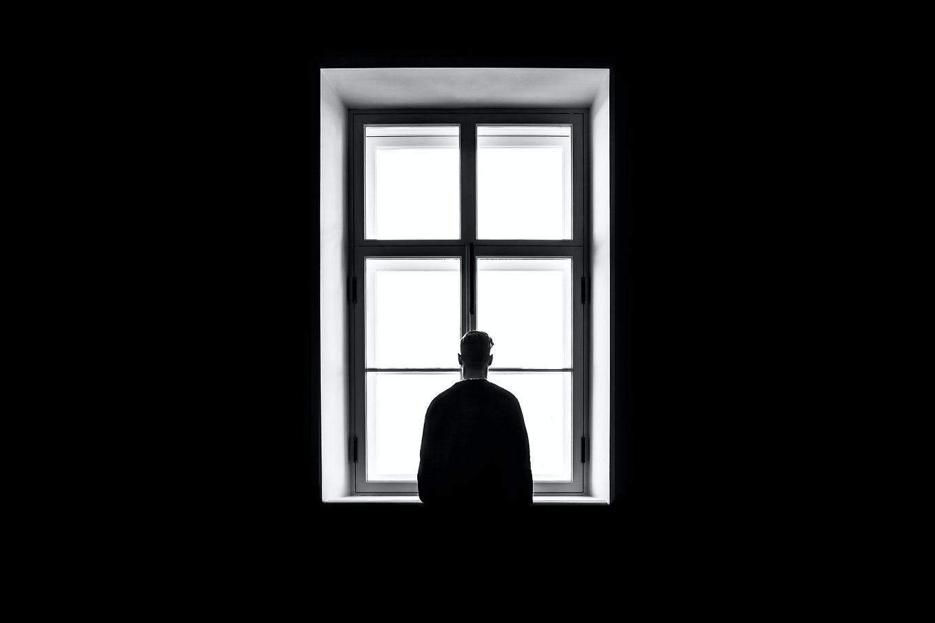 A man, standing in a dark room, staring out the window, alone. He’s probably fine.