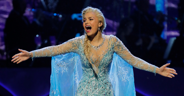 Samantha Barks performing as Elsa from Frozen, her mouth open and arms outstretched