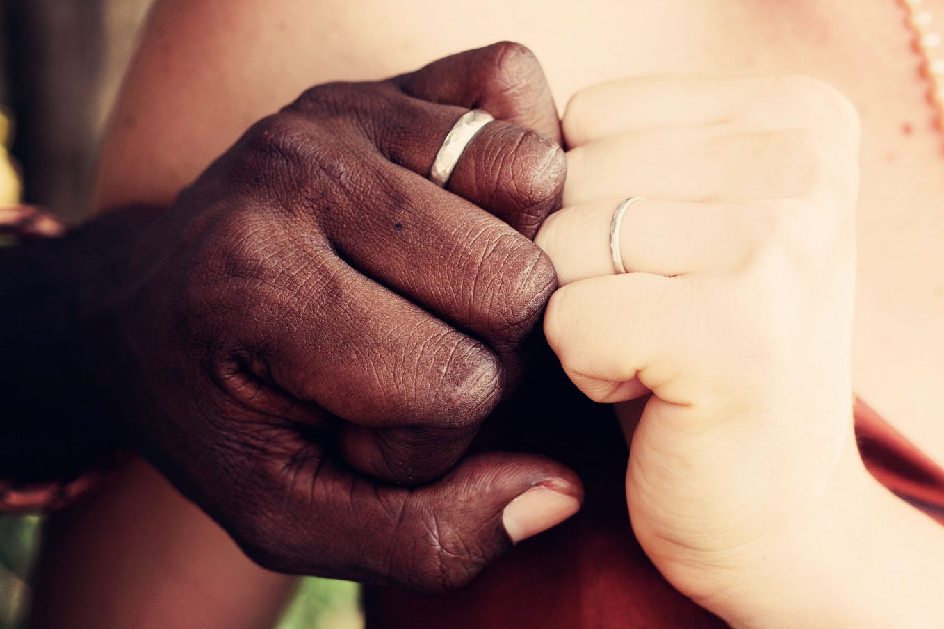 A Black man’s hand and a White woman’s hand coming together in a loving fist bump