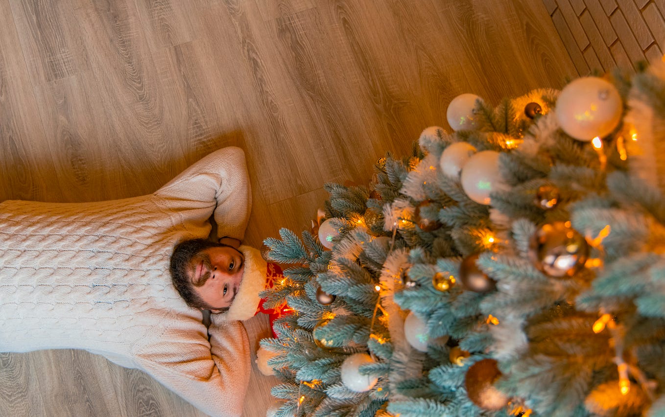 A man lays on his back looking up through the branches of a Christmas tree.