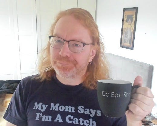 Chris Heilmann wearing a T-Shirt saying “My Mom says I’m a catch” and holding a cup saying “Do Epic Shit”