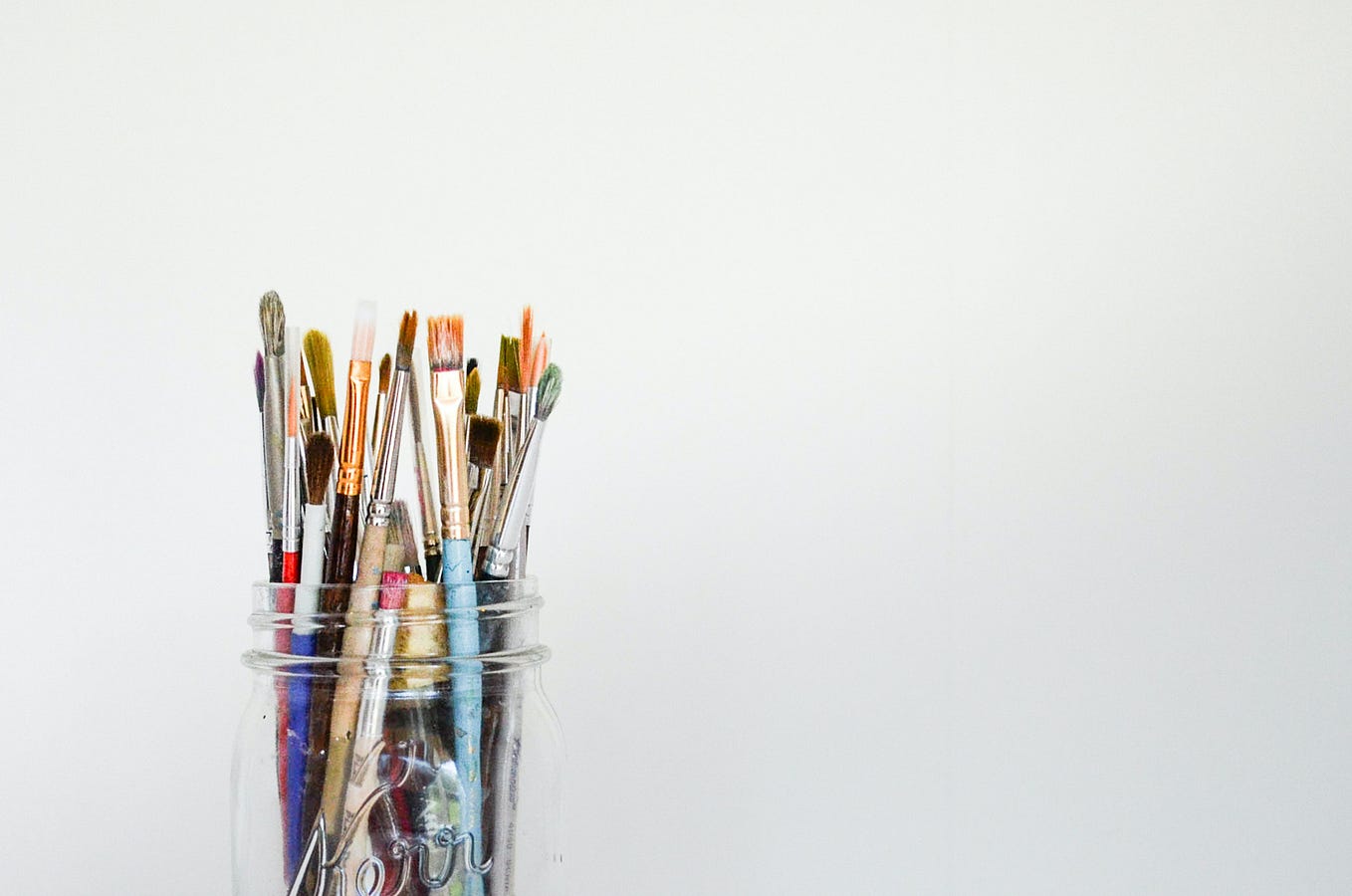 A jar of artists paintbrushes against a soft grey background