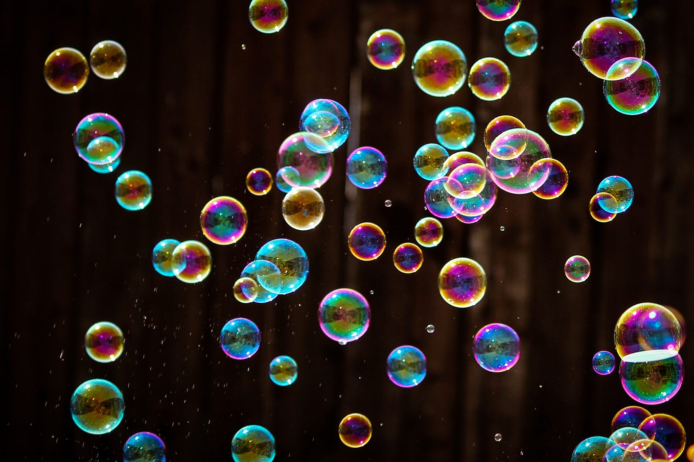 Many iridescent soap bubbles glimmering in darkness.
