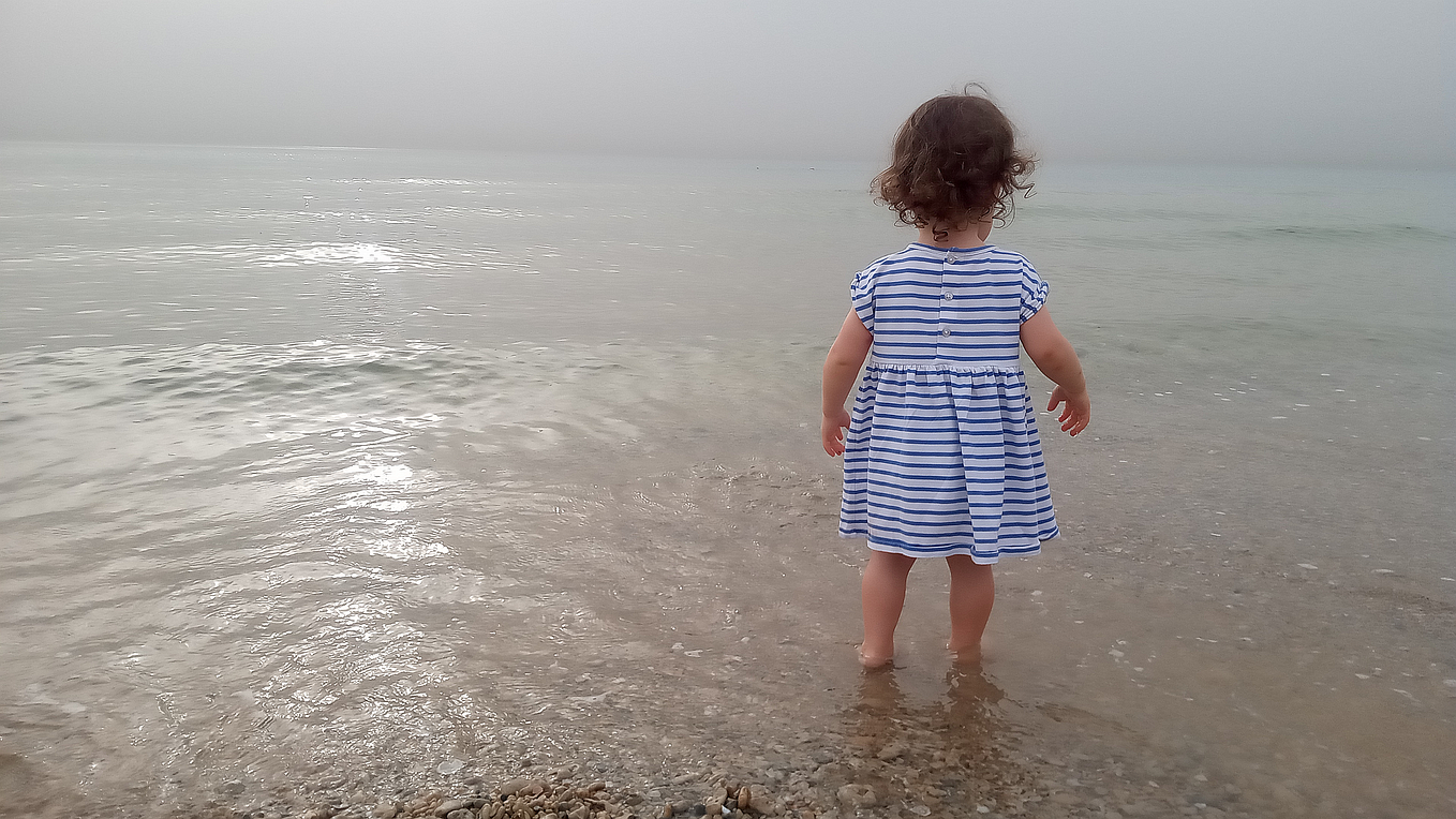 A young girl in blue-white striped dress standing in the shallow waters.