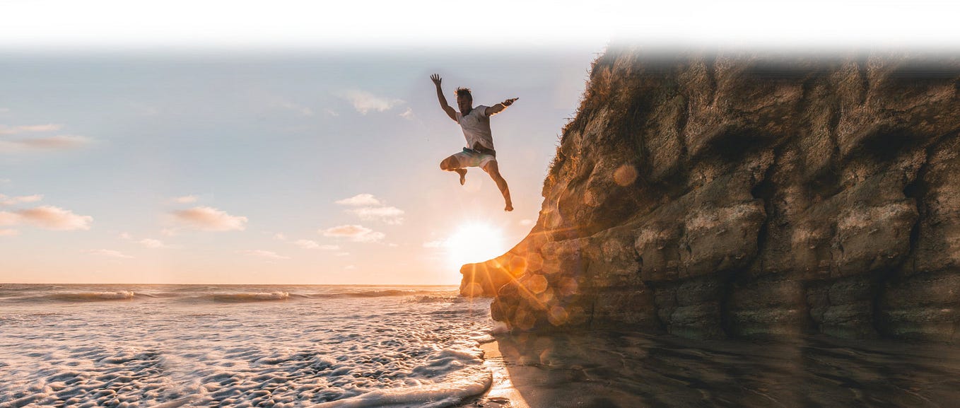 A guy jumping off a cliff into the water at sunset