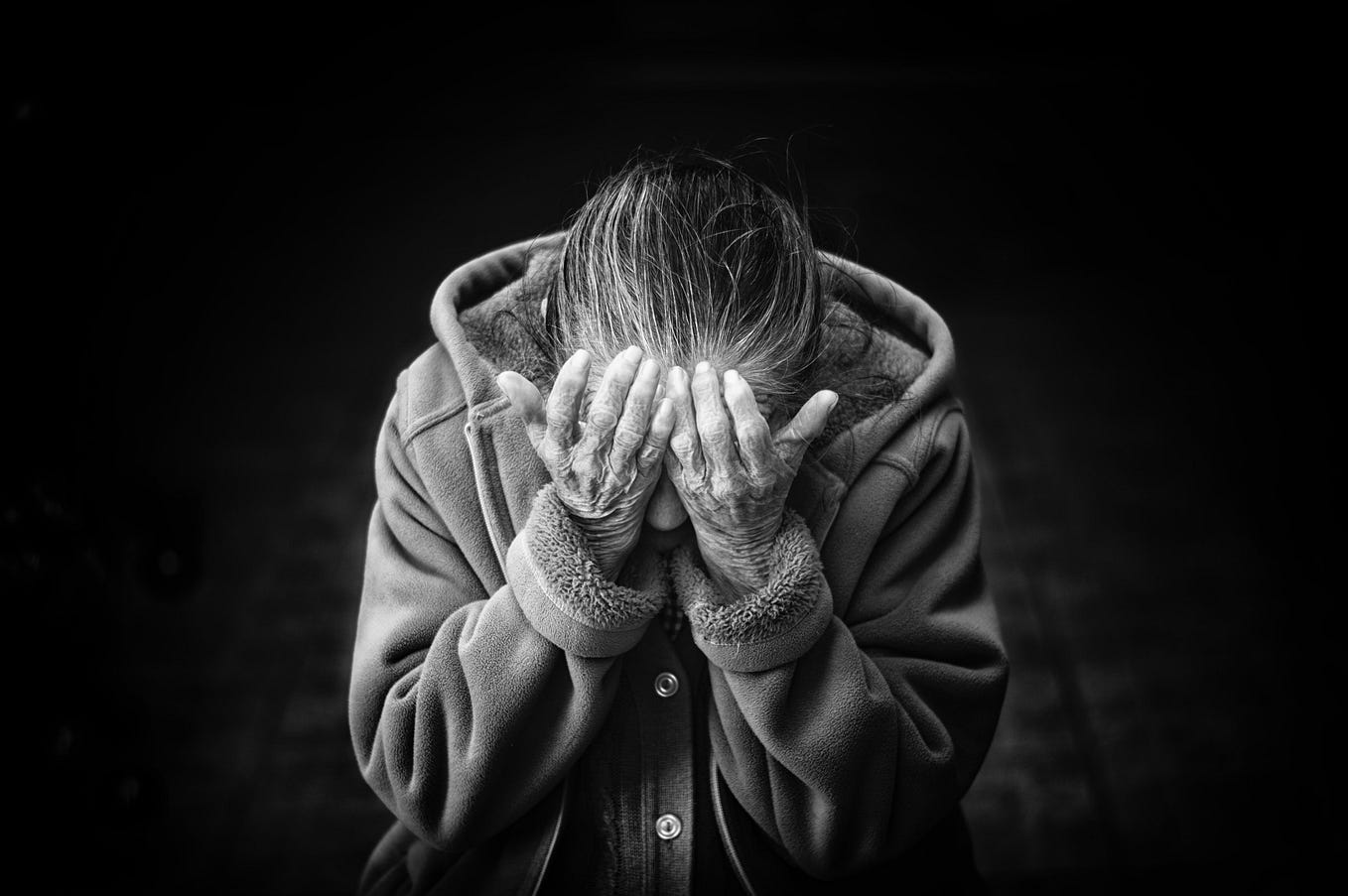 Black and white image of person wearing a sweatshirt holding their head in their hands. Their hair is long and tied back.