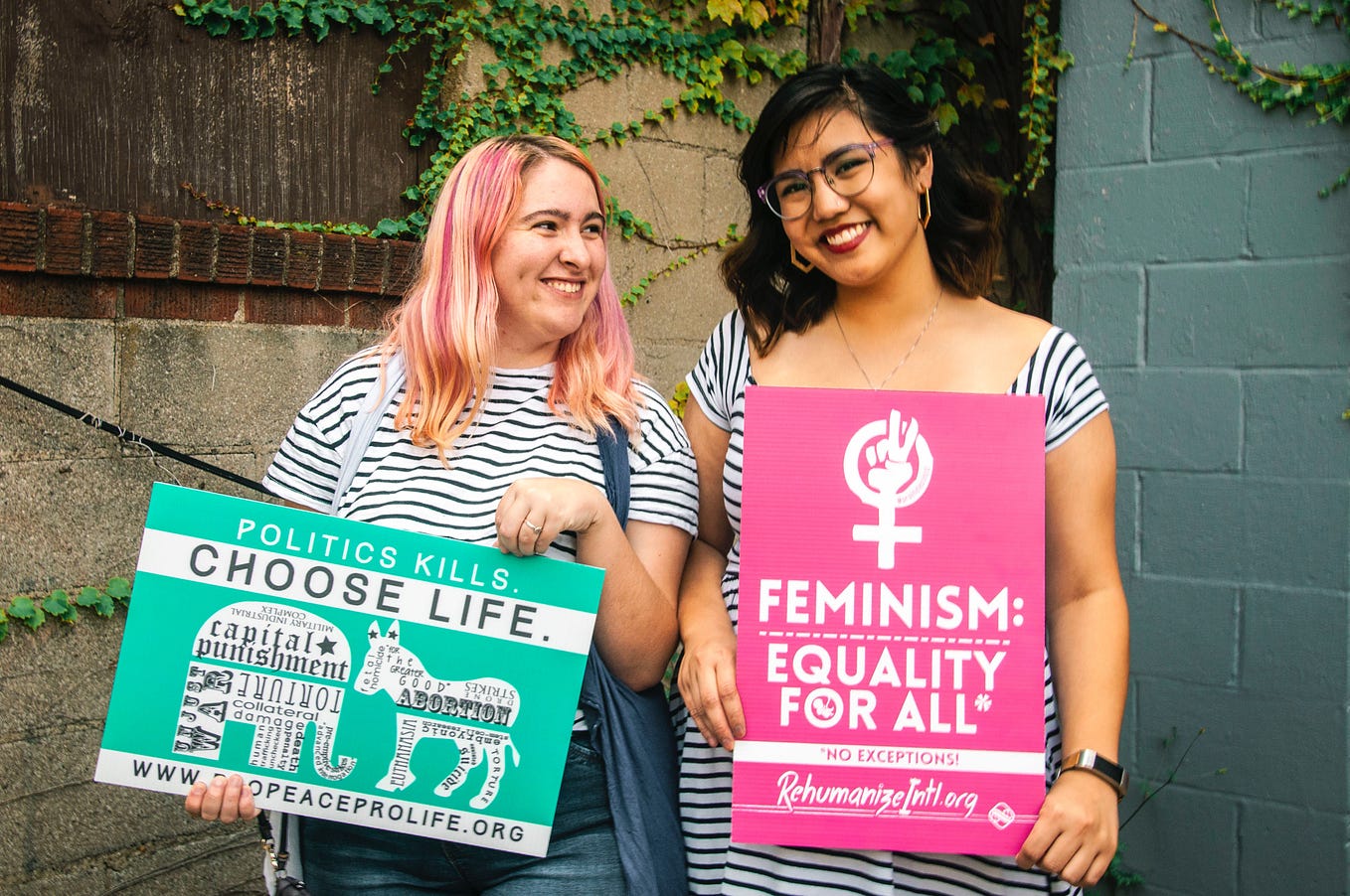 Image of two people, presumably women, holding signs supporting feminism and reproductive rights.