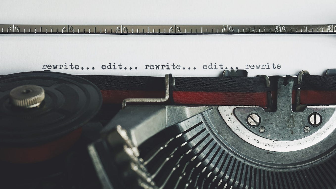 A close up of a manual typewriter with a page on the platten with the text “rewrite… edit… rewrite… edit… rewrite”