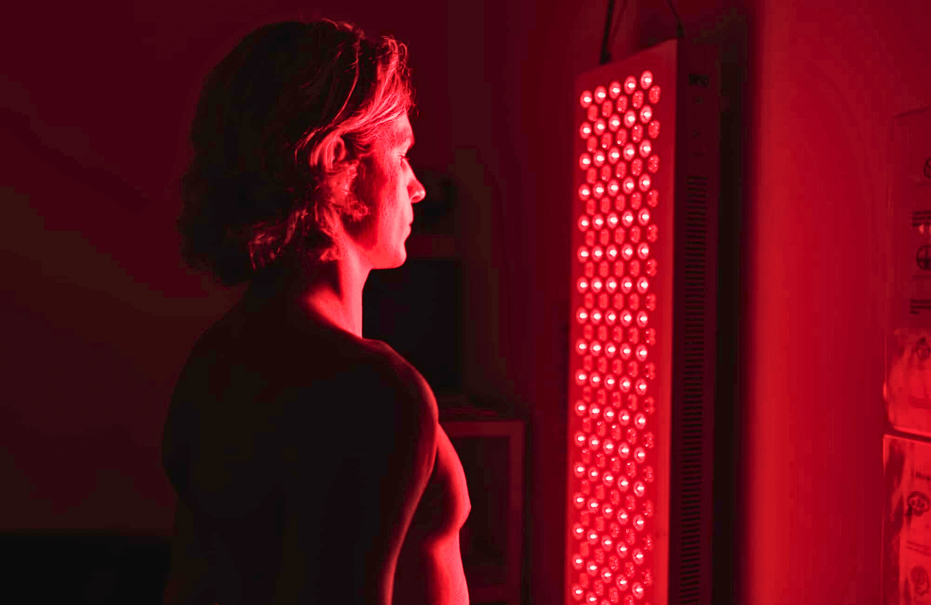 A person, standing in front of a red light therapy panel.