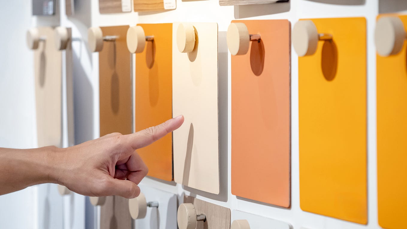 Designer hand pointing at colorful laminate sheet on material swatch wall display in material library.