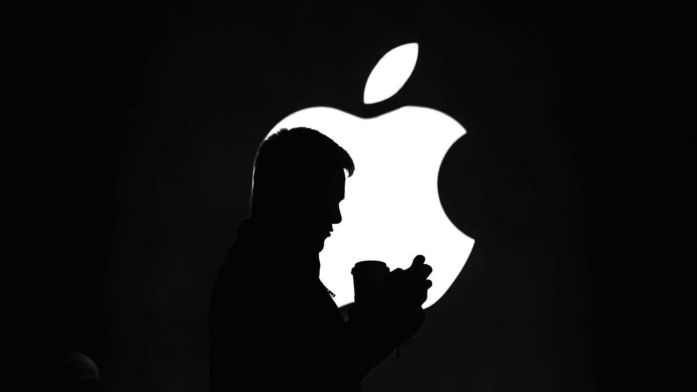 Silhouette of man using phone before a glowing Apple logo