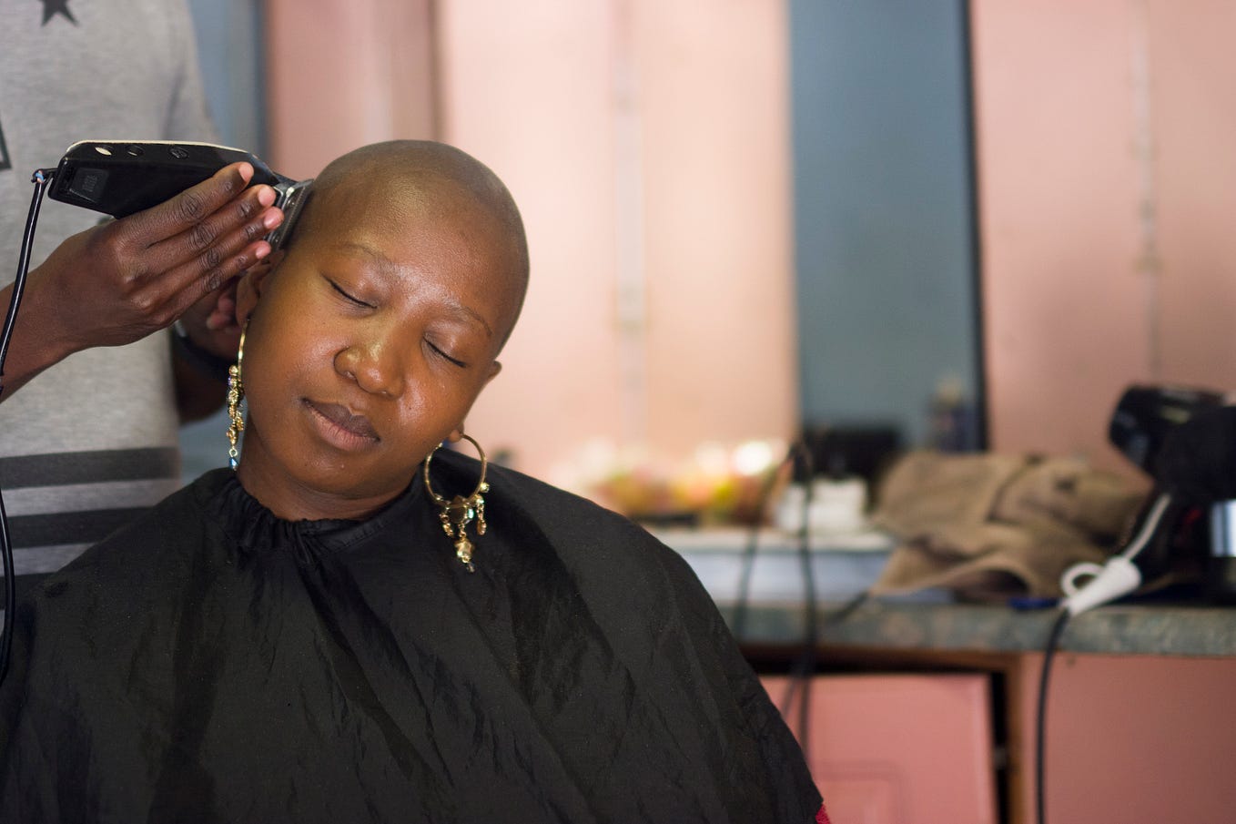 Black woman shaving her hair, with a peaceful expression.