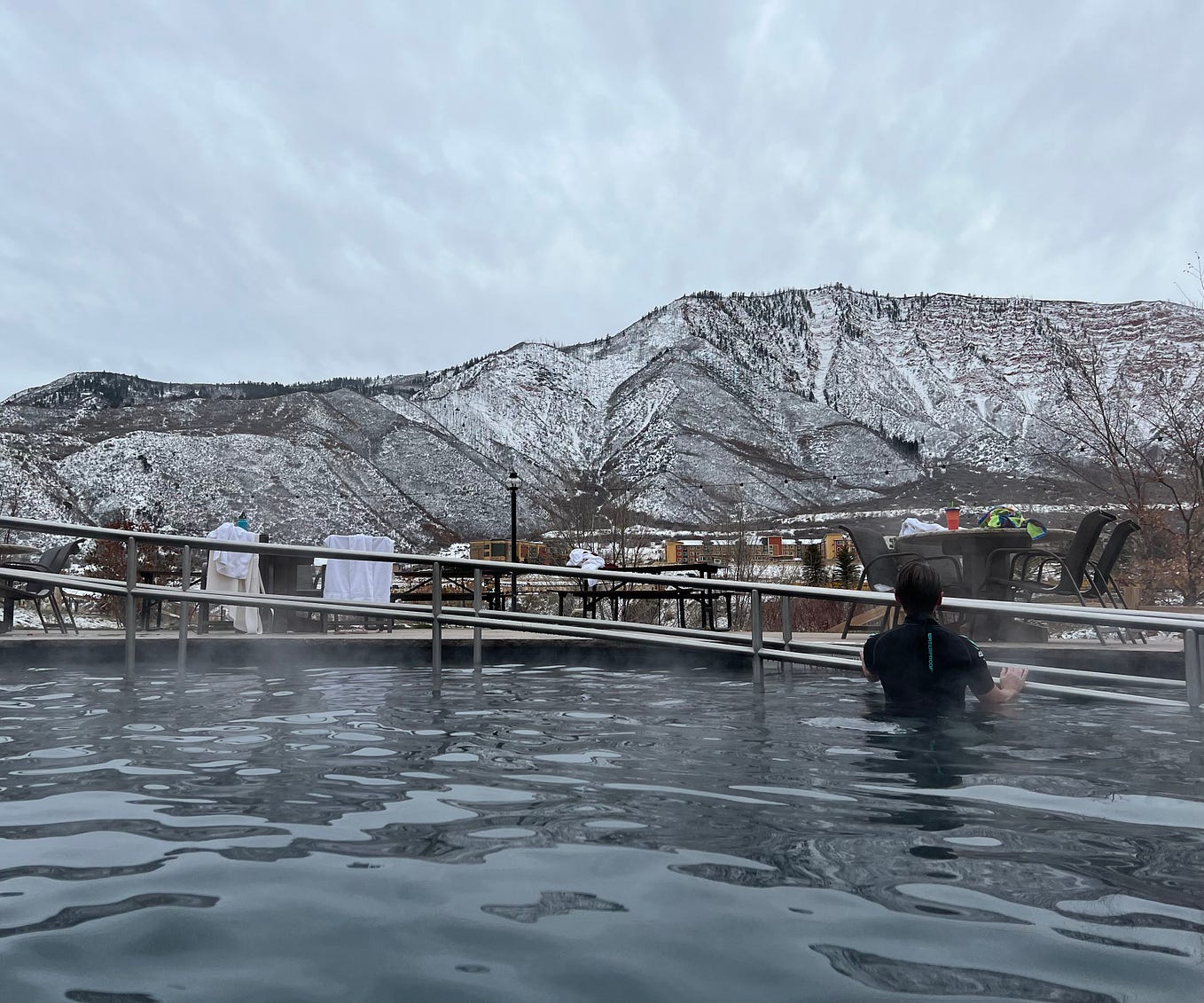 Author is staring at a snow-covered mountain from inside of a pool full of water from the hot springs.