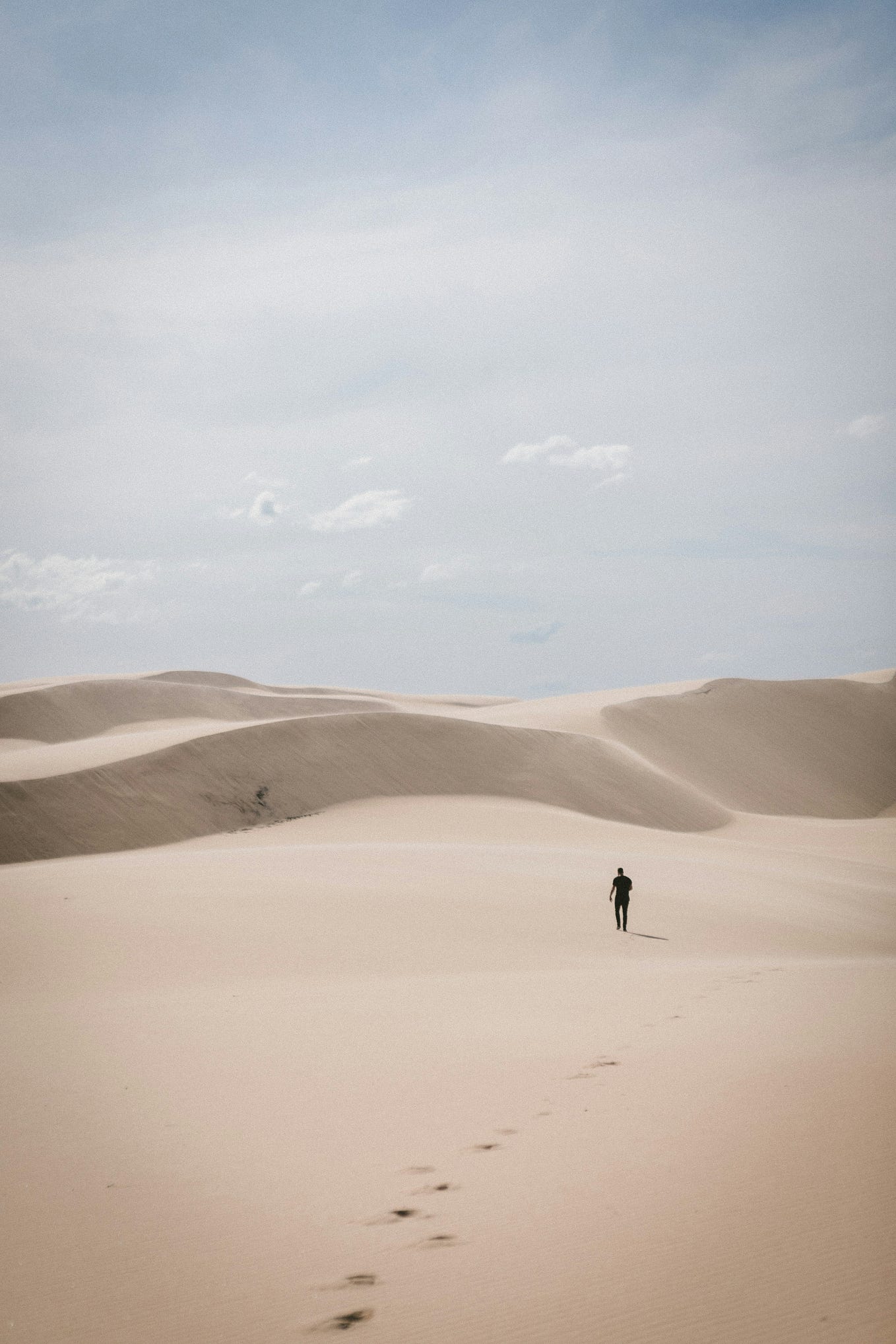 A lone man, walking away from viewer, in a long expanse of desert. A small shadow behind him.