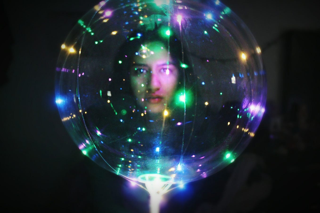 A photo of a woman with an illuminated transparent ball in a dark room.