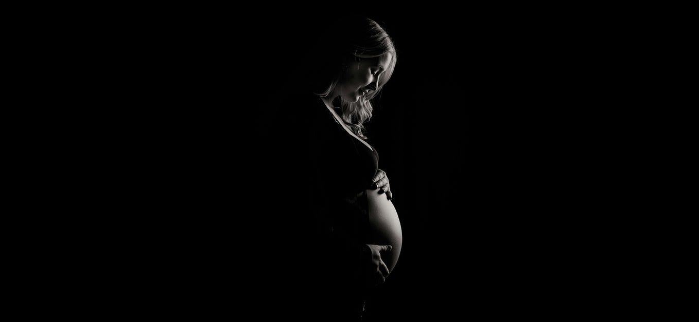 Pregnant young woman looking down at her bump which she is cradling with her hands.