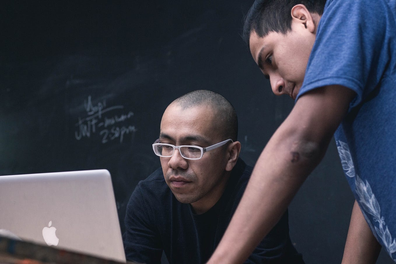 Two men in front of a blackboard looking at a laptop